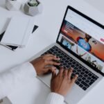 Mains d'une personne rédigeant du contenu sur un ordinateur portable posé sur un bureau blanc épuré.