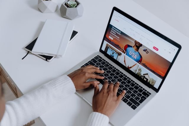 Mains d'une personne rédigeant du contenu sur un ordinateur portable posé sur un bureau blanc épuré.